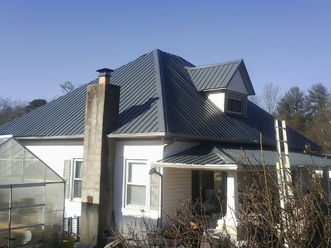 Dark blue standing seam metal roof on a white farmhouse with dormer — Slate & Tile Roof Repair by Roofing Brothers in Gold Hill