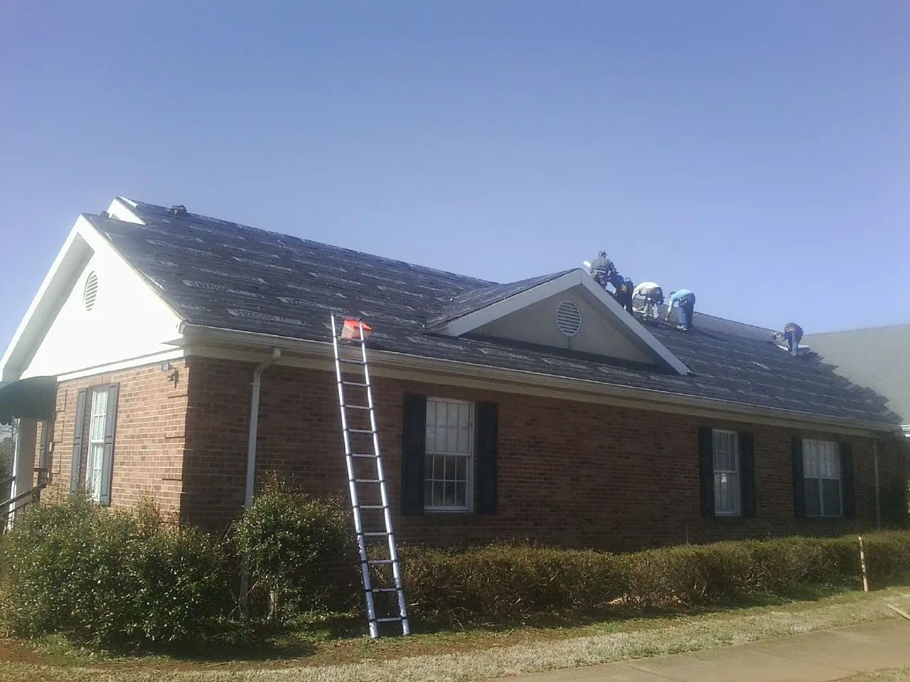 Crew tearing shingles off a brick ranch roof with a ladder set — Emergency Roof Repair work by our crew in Gold Hill
