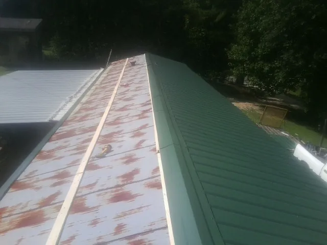 Old rusted panels beside newly installed green metal roofing — Wind Damage Roof Repair by Roofing Brothers in Gold Hill