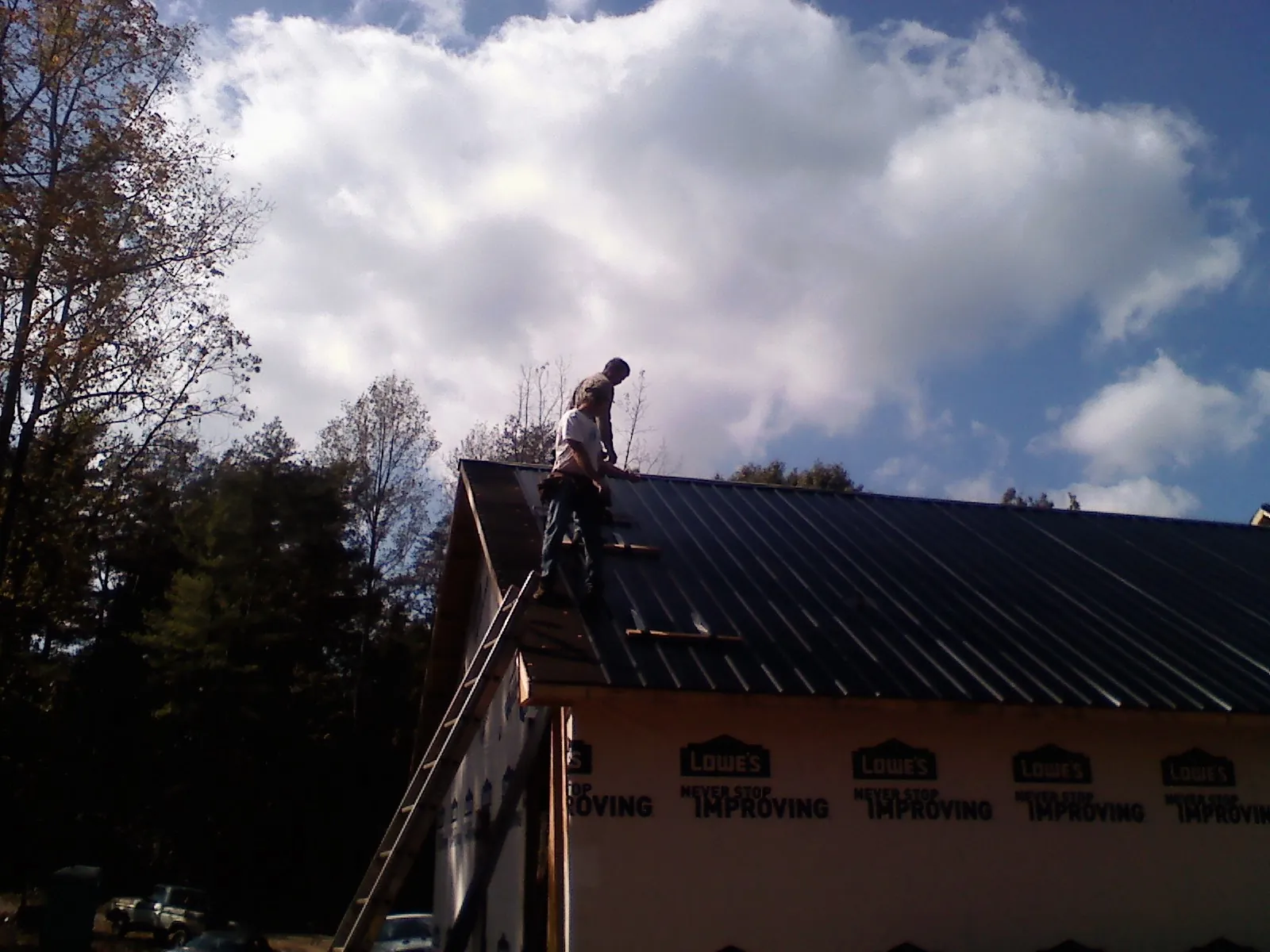 Roofer fastening dark metal panels high against a cloudy sky, from a Roof Inspection job in Gold Hill